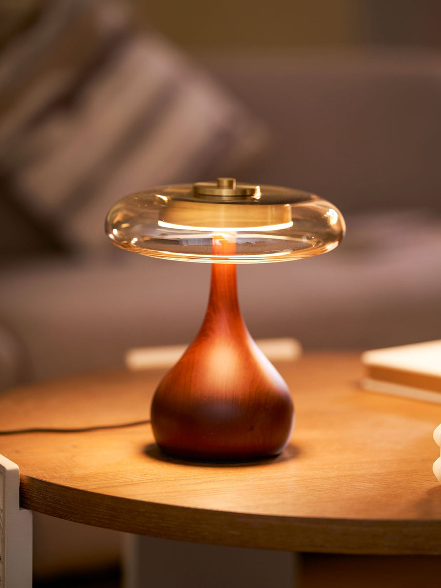 Table lamp with a glass shade lit on a round wood table at dusk