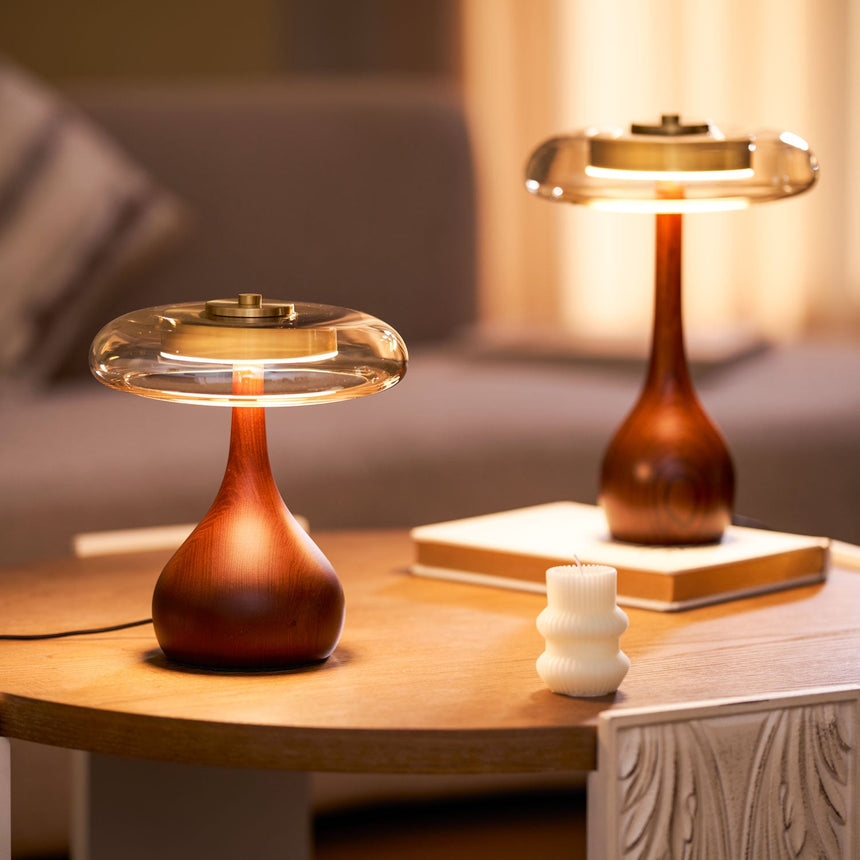 Table lamp with a glass shade lit on a nightstand beside a made bed