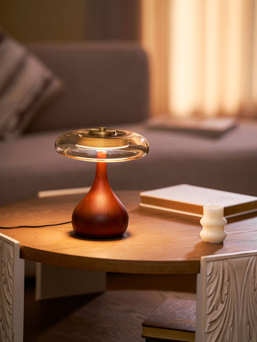Table lamp with a glass shade lit on a round wood table with books