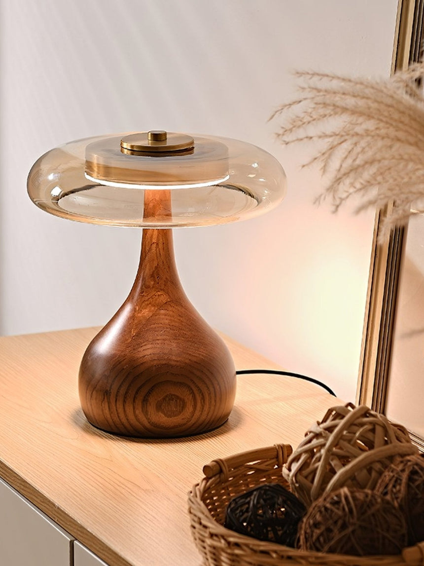 Table lamp with a glass shade lit on a sideboard beside dried grass