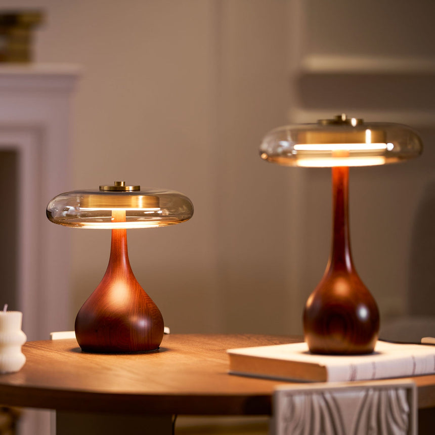 Two table lamps with glass shades lit on a long wood console