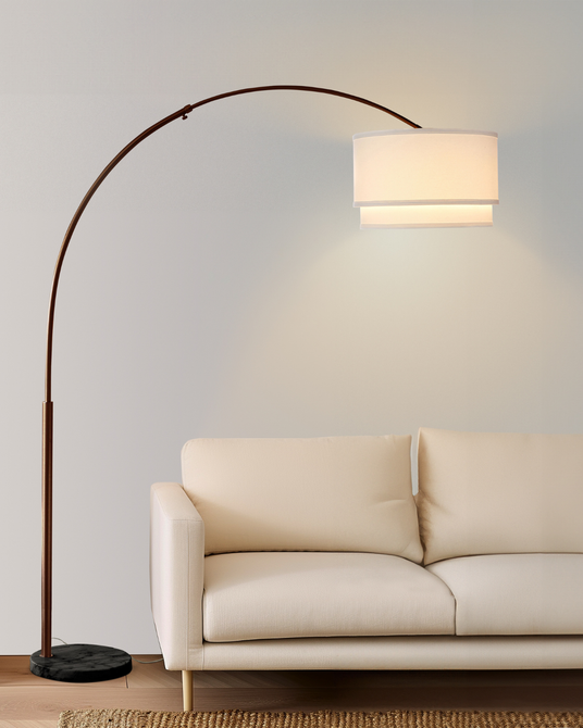 Bronze arc lit beside a cream sofa on a wood floor, shade over the seat