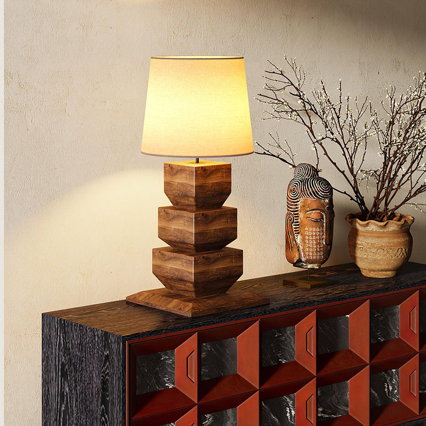Tall table lamp lit on a dark console beside branches in a stone vase