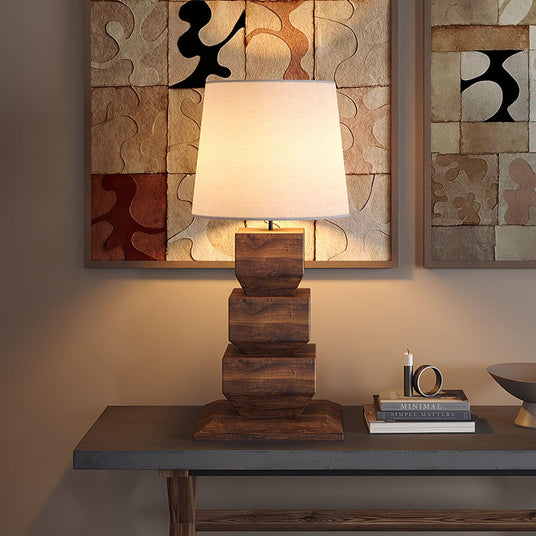 Tall table lamp lit on a console in front of a large abstract painting