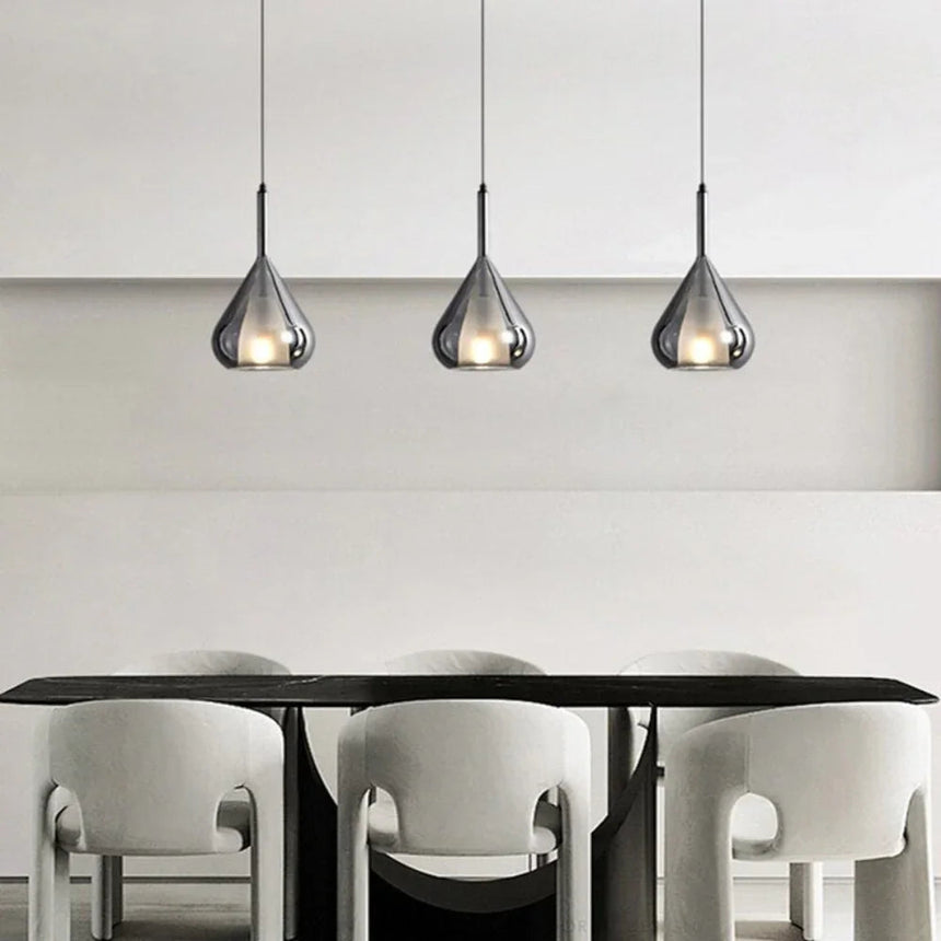 Three teardrop shades in a row above a dining table and pale chairs
