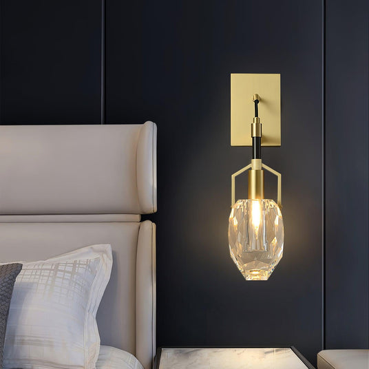 The crystal drop lit on a dark wall beside a white upholstered headboard