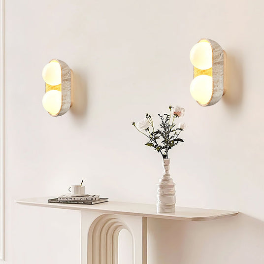 Two sconces lit on a wall above a fluted console holding a vase of flowers