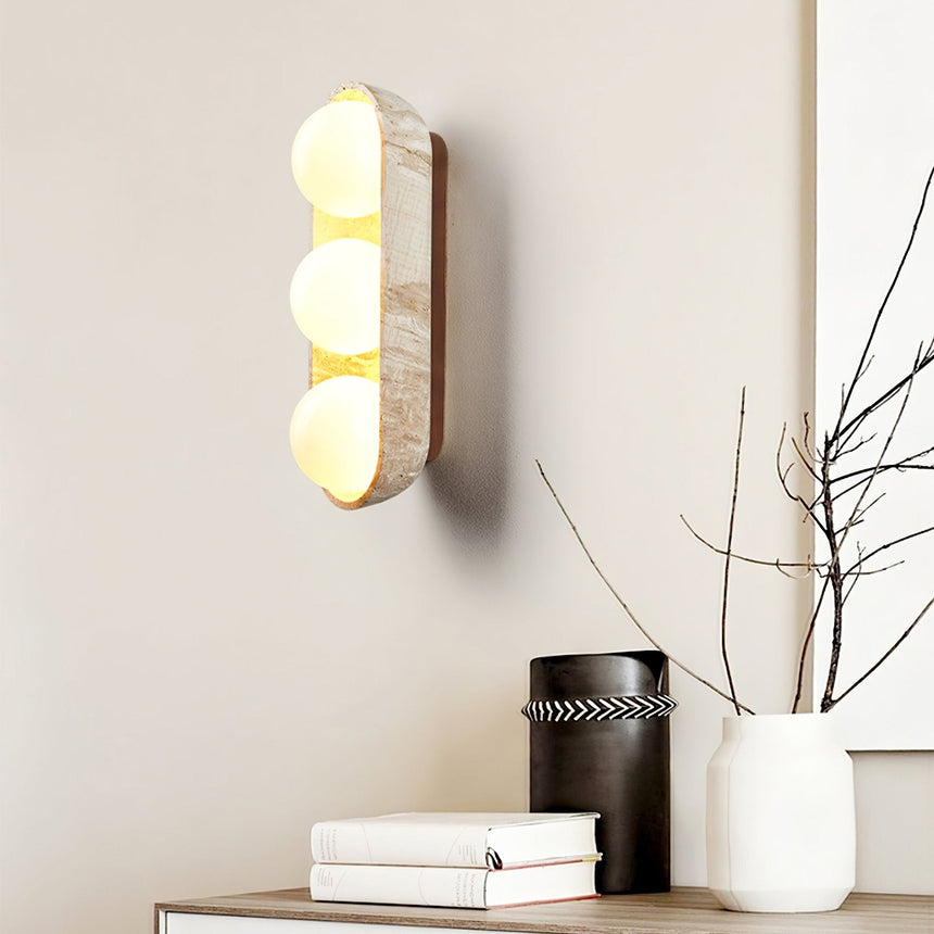 Sconce lit above a sideboard with books, a canister and a vase of branches