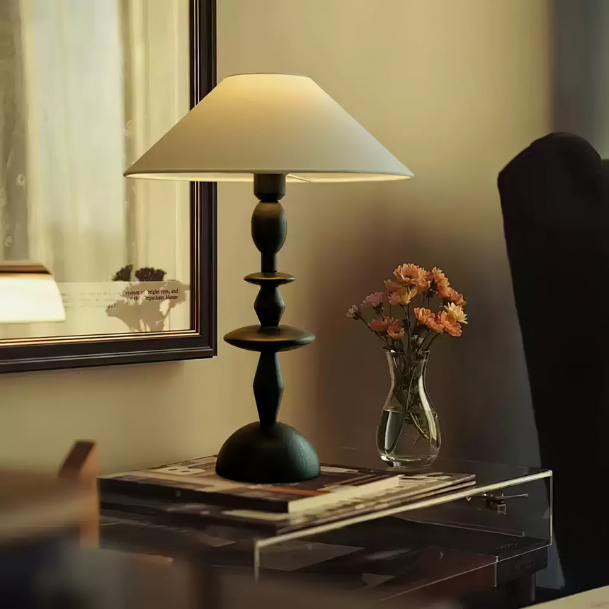 Spindle table lamp lit on a console beside a small vase of orange flowers