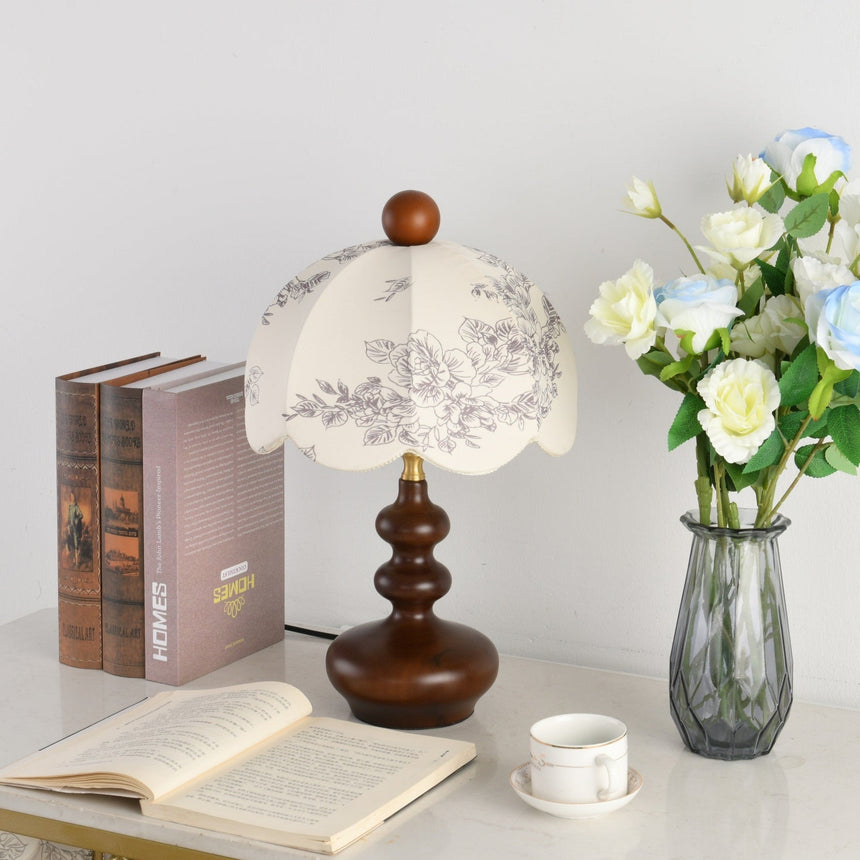 Toile shade lamp unlit beside cream roses in a glass vase