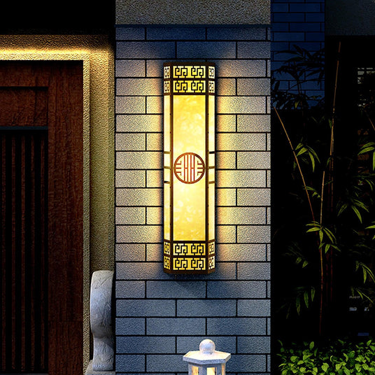 The column light glowing on a gray brick wall beside a wood front door and bamboo