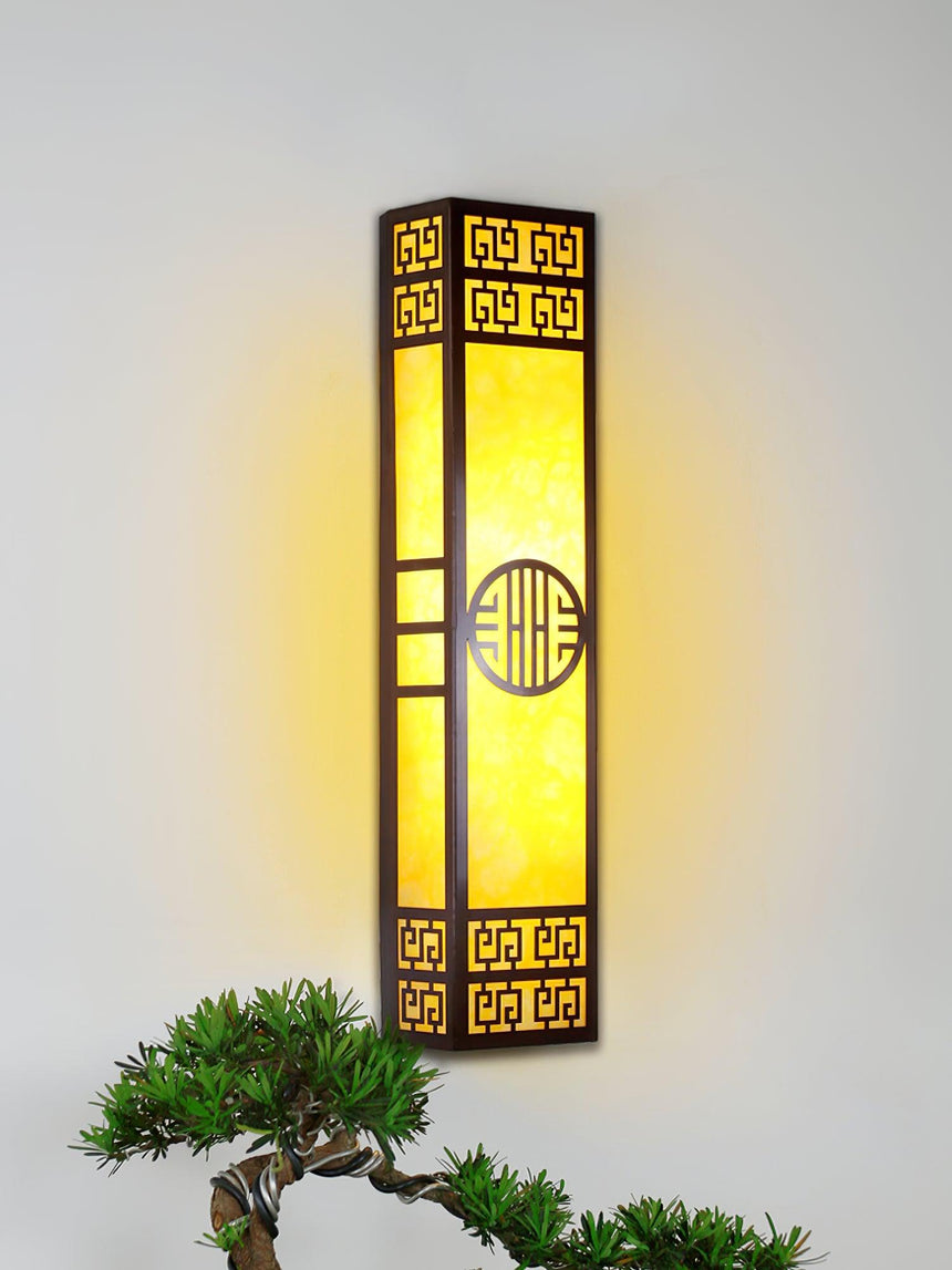 The lit column on a pale wall above a small clipped pine in a garden