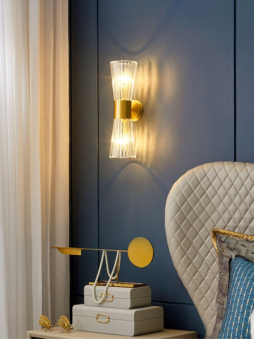 The sconce on a blue wall above a desk with a lamp beside a quilted chair
