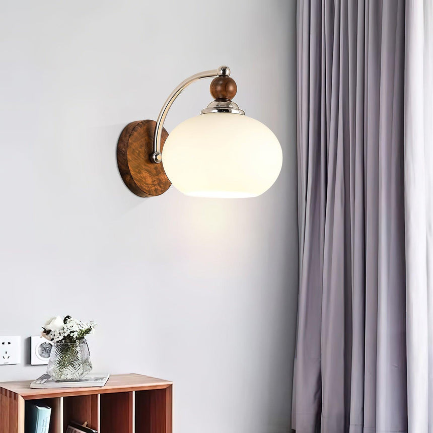 Sconce lit beside a curtain above a low cabinet holding a glass vase