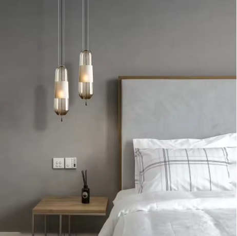 Two tube pendants hung beside a bed with a wooden headboard and shelf