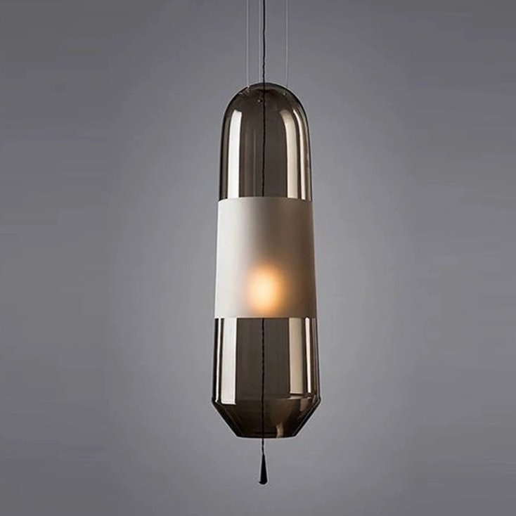 A smoke gray glass tube pendant lit against a pale gray wall