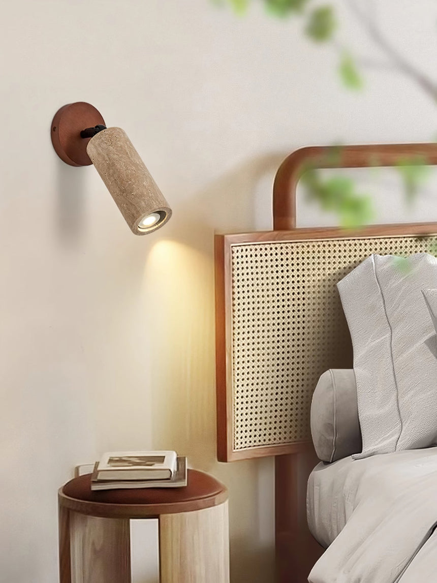 Travertine tube lit on a bedside wall next to a rattan headboard