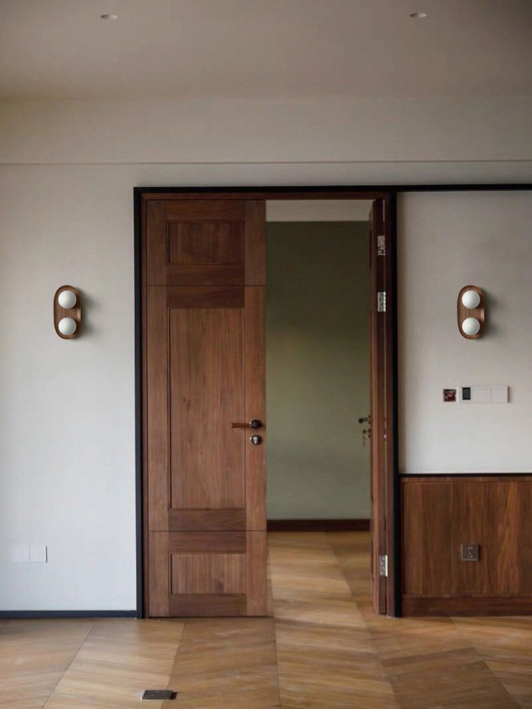 Two sconces lit either side of a wood doorway in a hallway with a floor