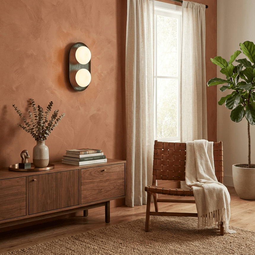 Sconce lit on a terracotta wall above a sideboard with a vase and books