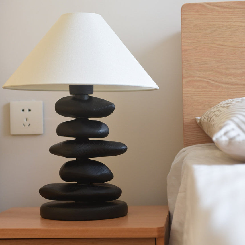 Unique table lamp in matte black on a nightstand beside a bed