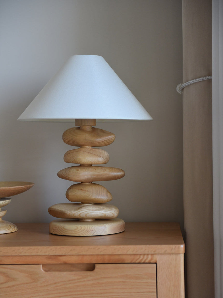 Unique table lamp in light wood on a dresser beside a wall