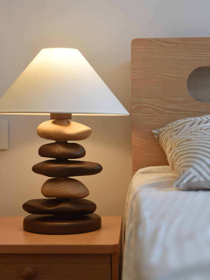 Unique table lamp with a mixed stack lit beside a woven headboard