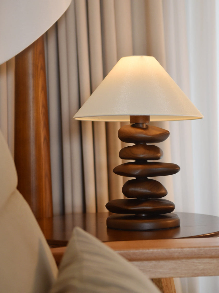 Unique table lamp lit on a side table in front of pale curtains