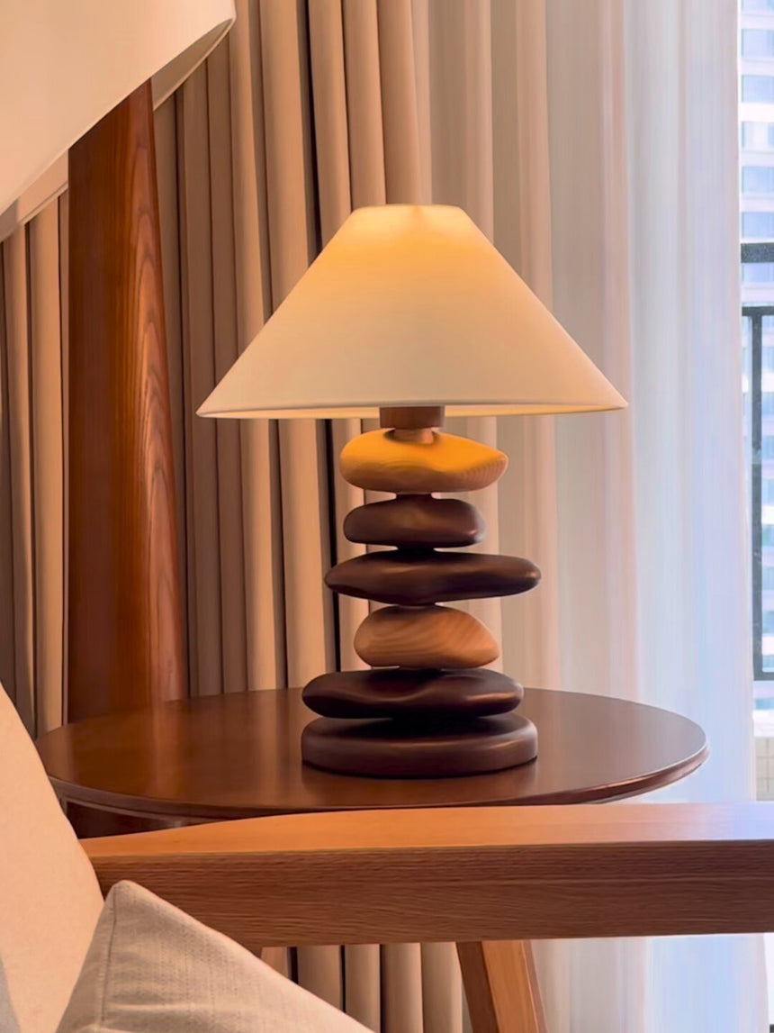 Unique table lamp lit on a round wood table beside a curtain