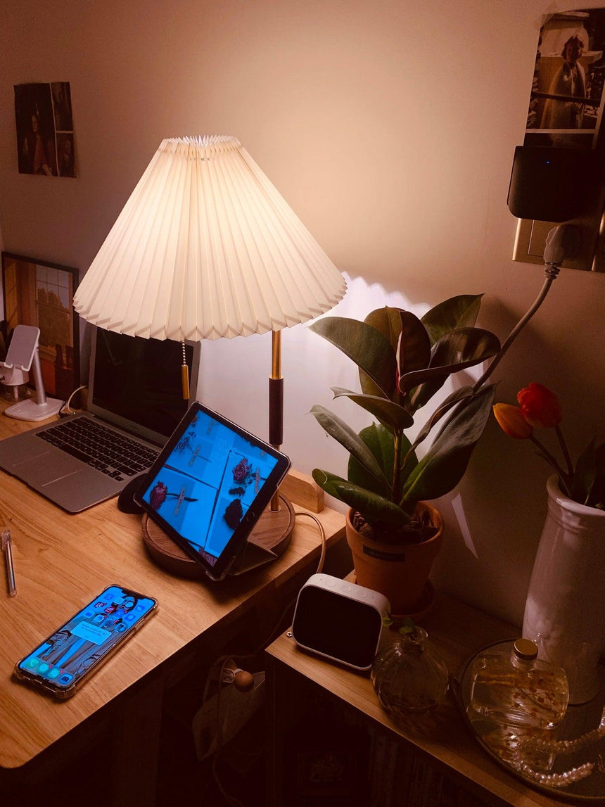 Table lamp lit on a home desk at night beside a laptop and a plant