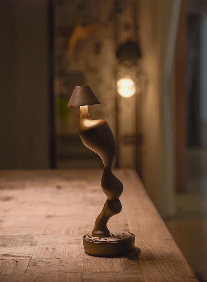 Cordless carved wood table lamp lit on a wooden surface against a wall