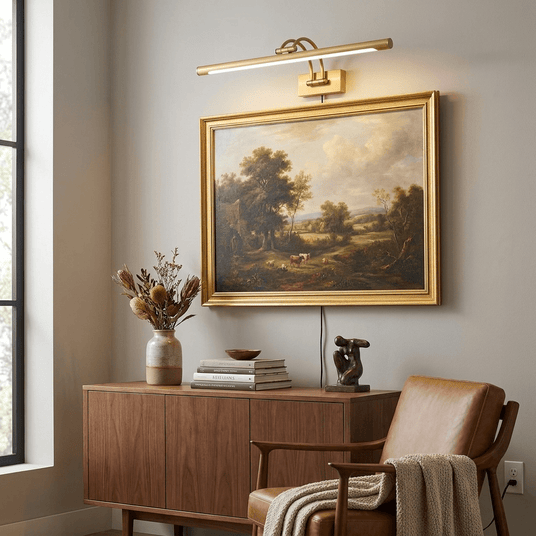 Brass bar lit over a gilt framed landscape painting above a walnut sideboard and a chair
