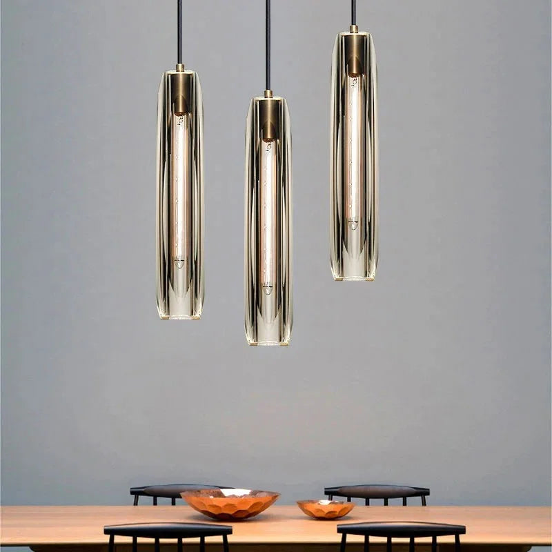 Three slim copper and glass pendants lit above a wooden sideboard