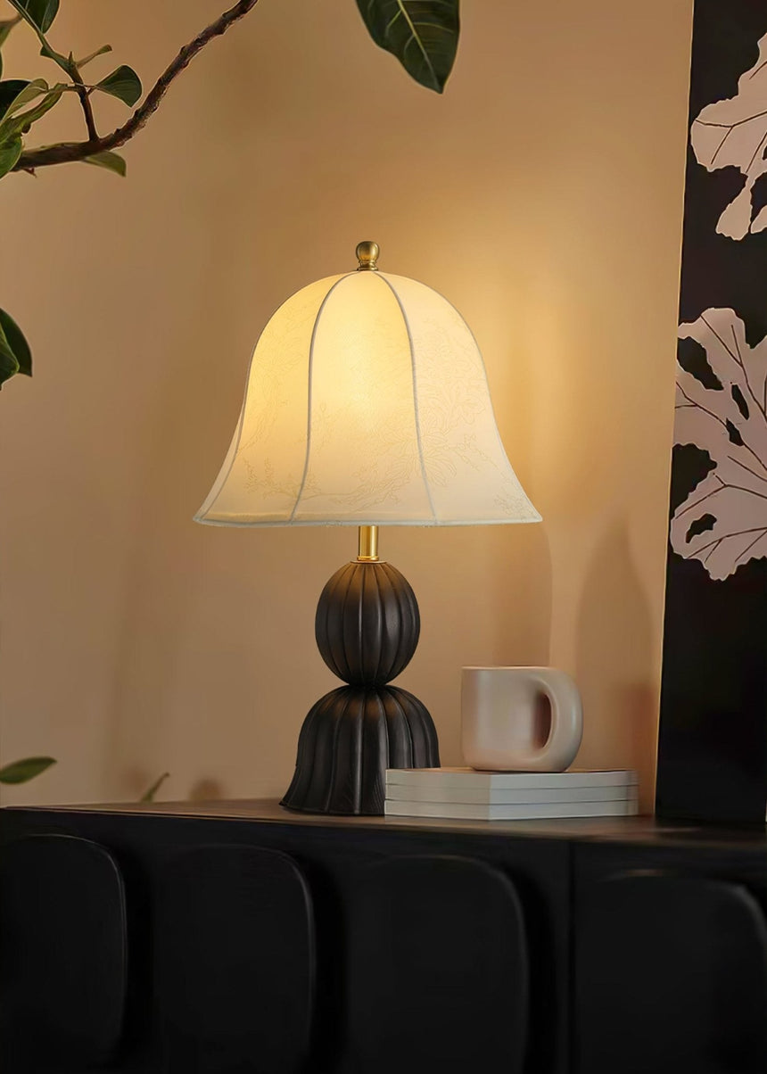 Black based vintage table lamp lit on a dark unit beside a white mug