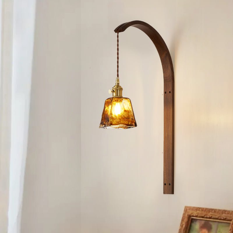 Amber glass shade lit warm on the wood arm beside a curtain and a frame