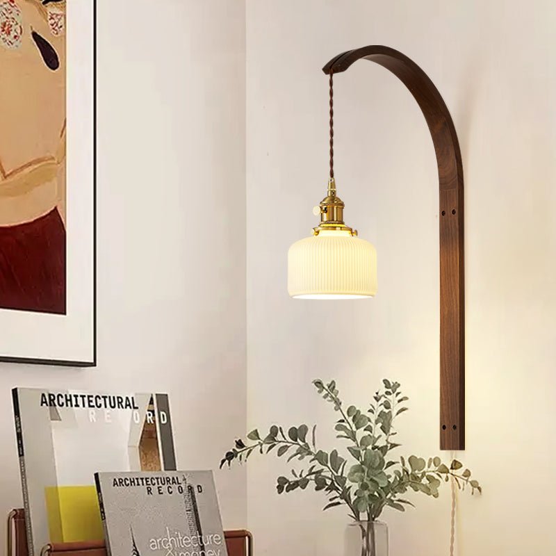Lamp lit beside a bed with framed prints leaning on a shelf and a plant