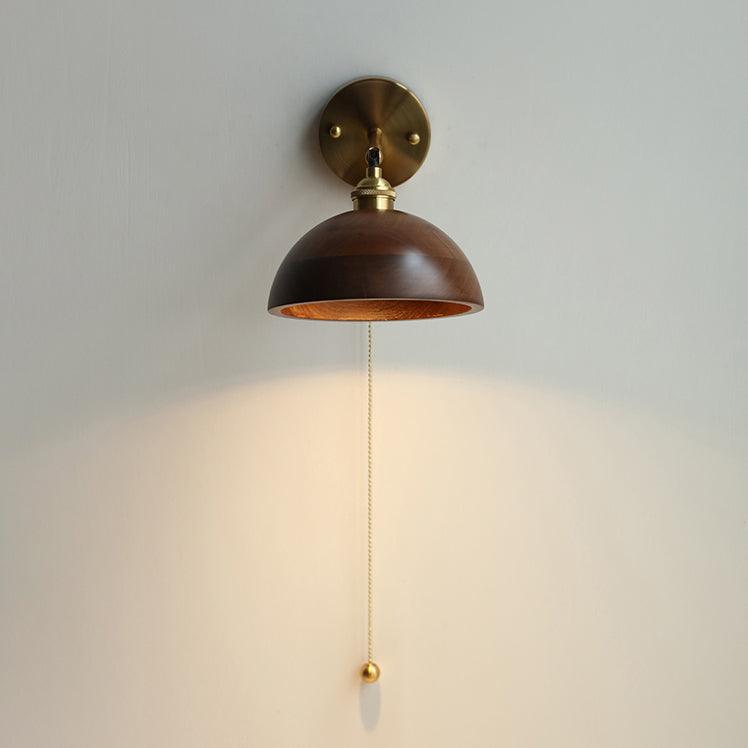 Rounded walnut dome sconce unlit, the brass pull cord hanging below