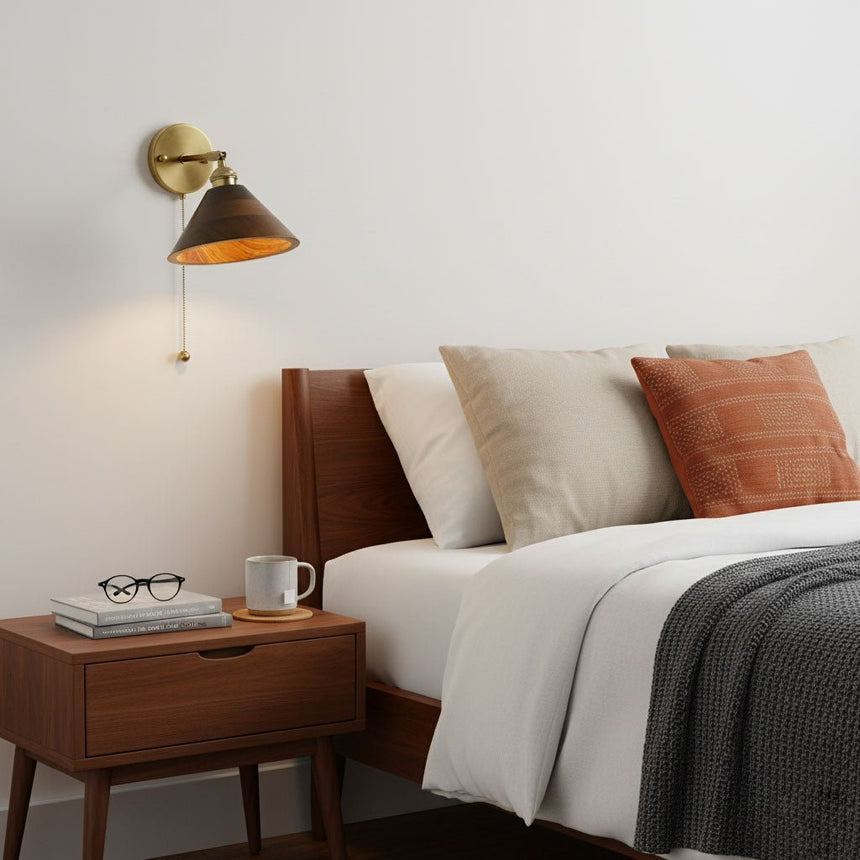 Walnut dome sconce lit above a nightstand beside a made bed