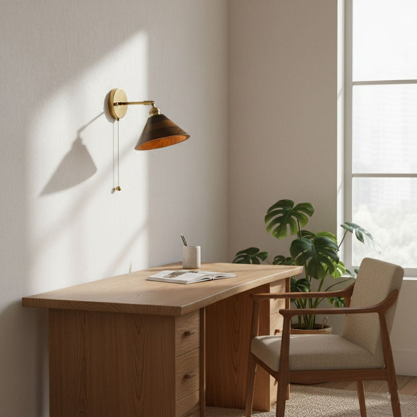 Walnut sconce lit above a wood desk with a plant and a chair