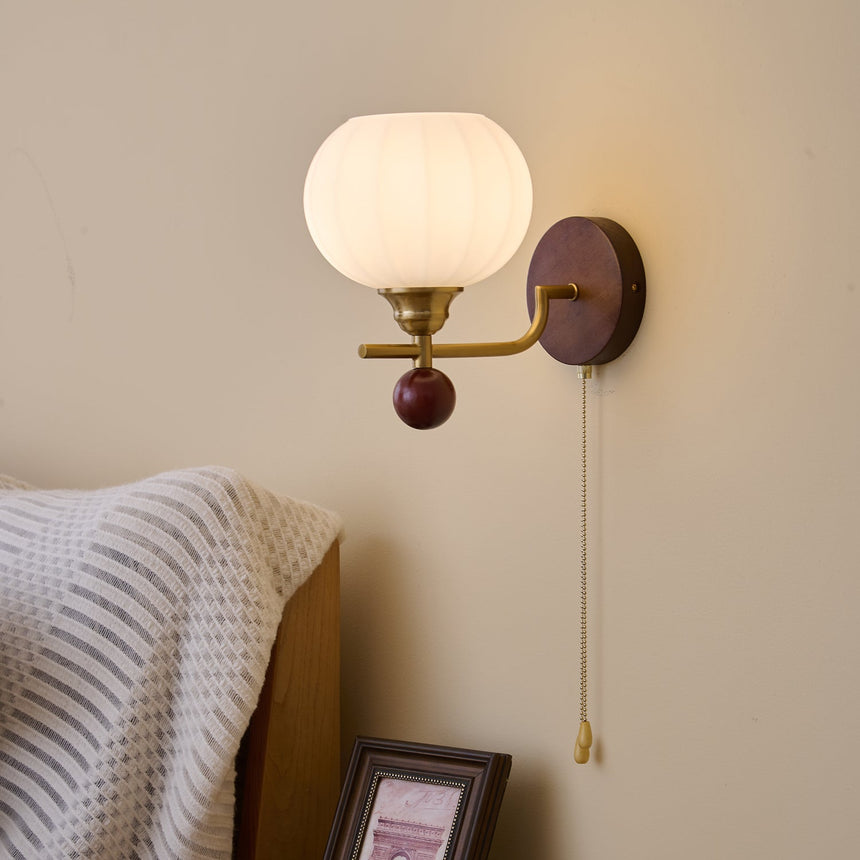 Ribbed glass sconce lit above a bed beside a small framed picture