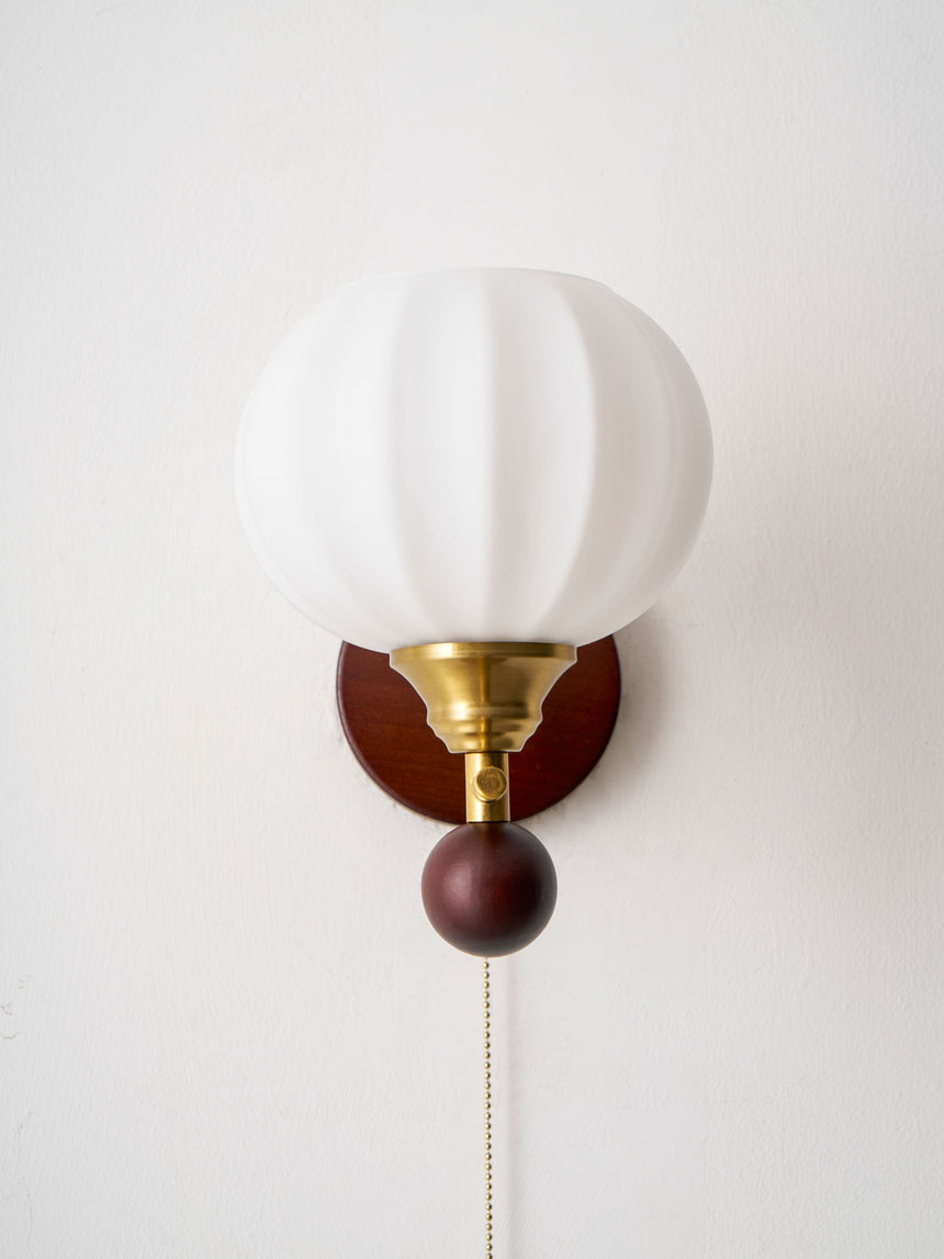 Ribbed white glass globe lit warm on its brass arm and wood plate