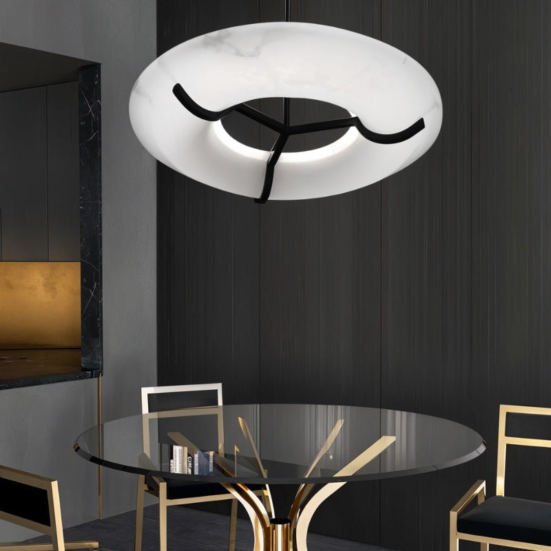 The lit ring above a glass dining table with gold chairs in a dark room