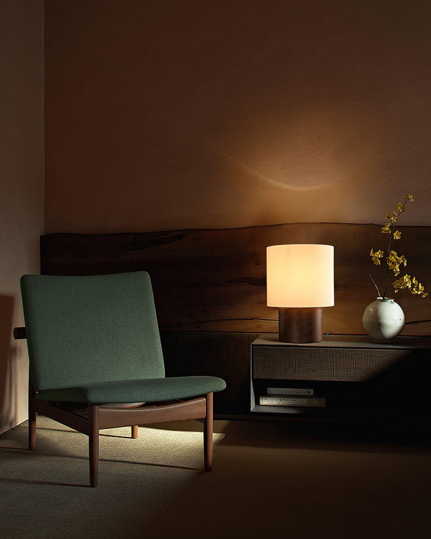 Wabi sabi table lamp lit on a table beside a green armchair