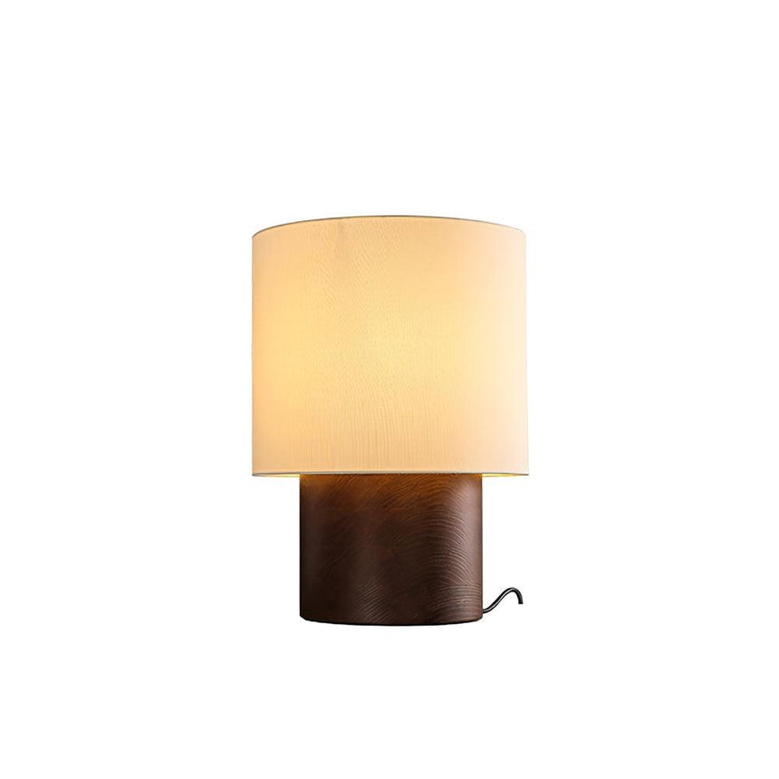 Wabi sabi table lamp in walnut lit against a plain pale ground
