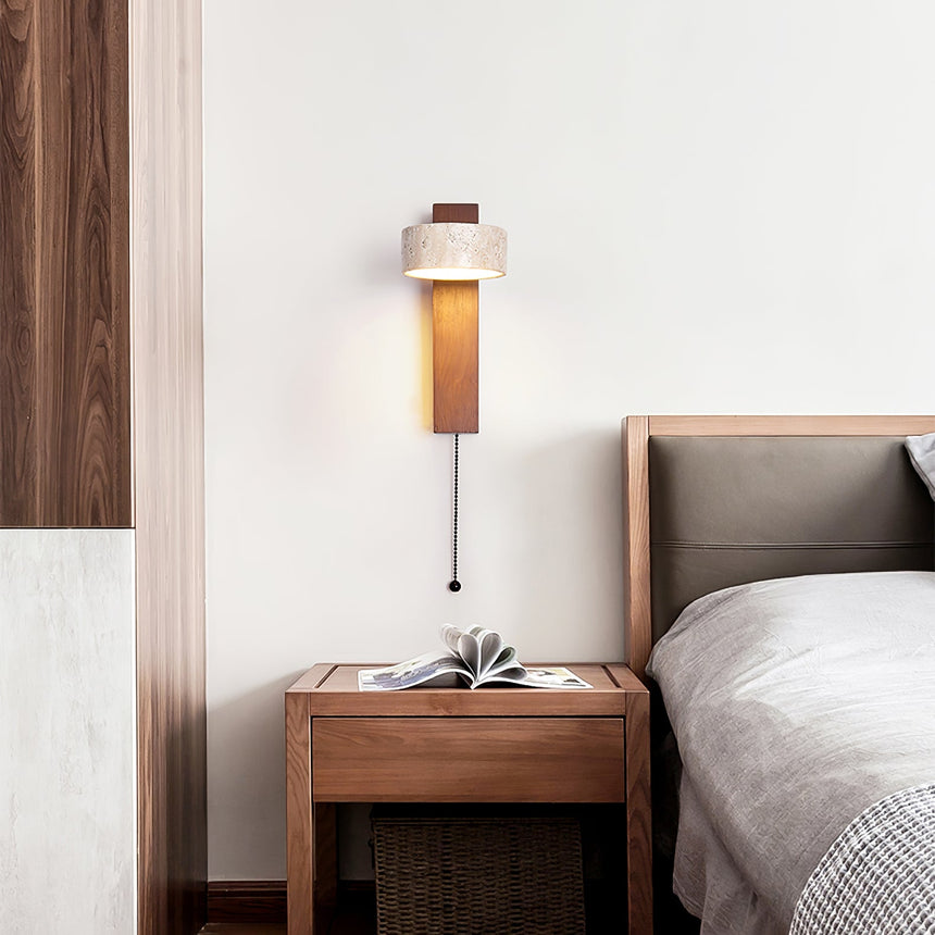 Lamp lit beside a bed above a nightstand holding a plant in a stone pot
