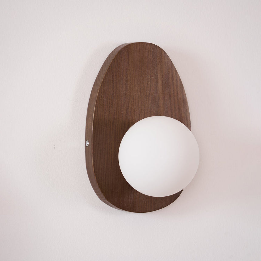 Walnut oval sconce seen at an angle, the glass sphere proud of the plate