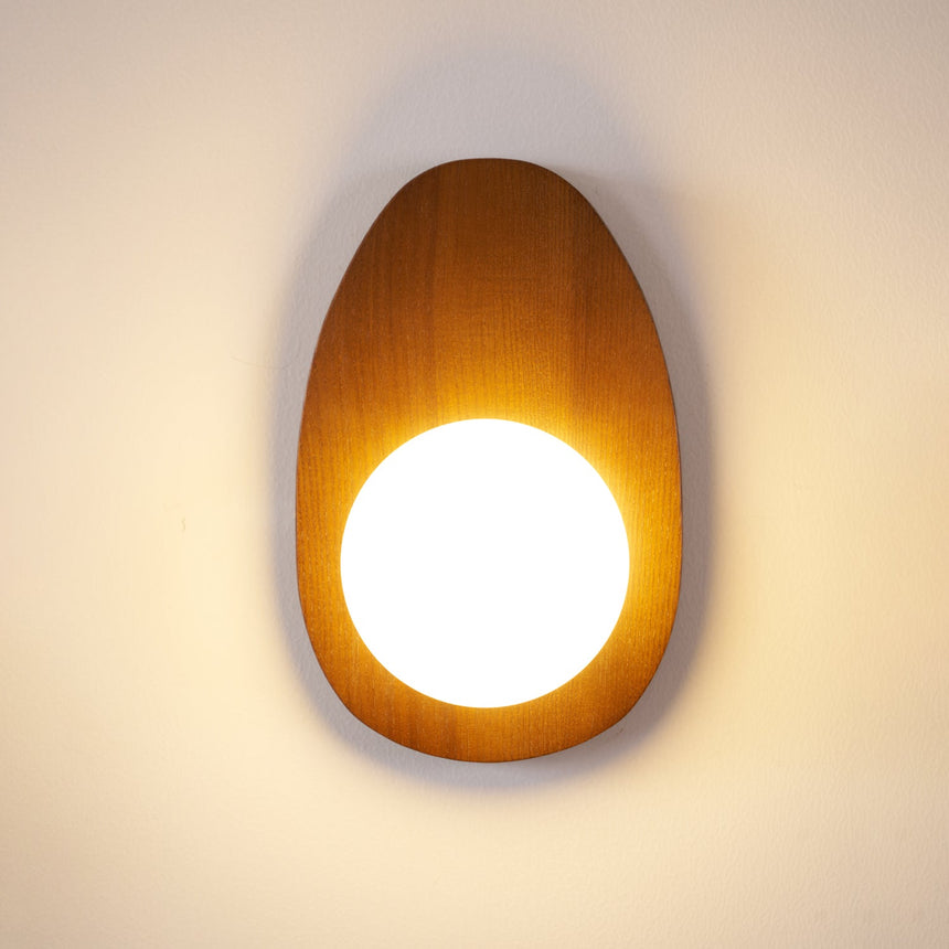 The sconce lit in a dark room, warm light spreading across the wall