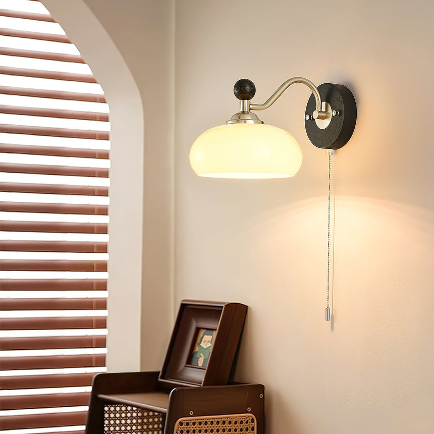 Lamp lit beside a slatted shutter above a cane chair and a framed print