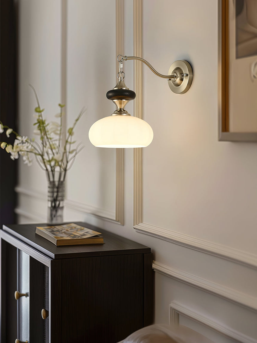 Lamp lit on a panel wall above a dark cabinet with a vase of stems