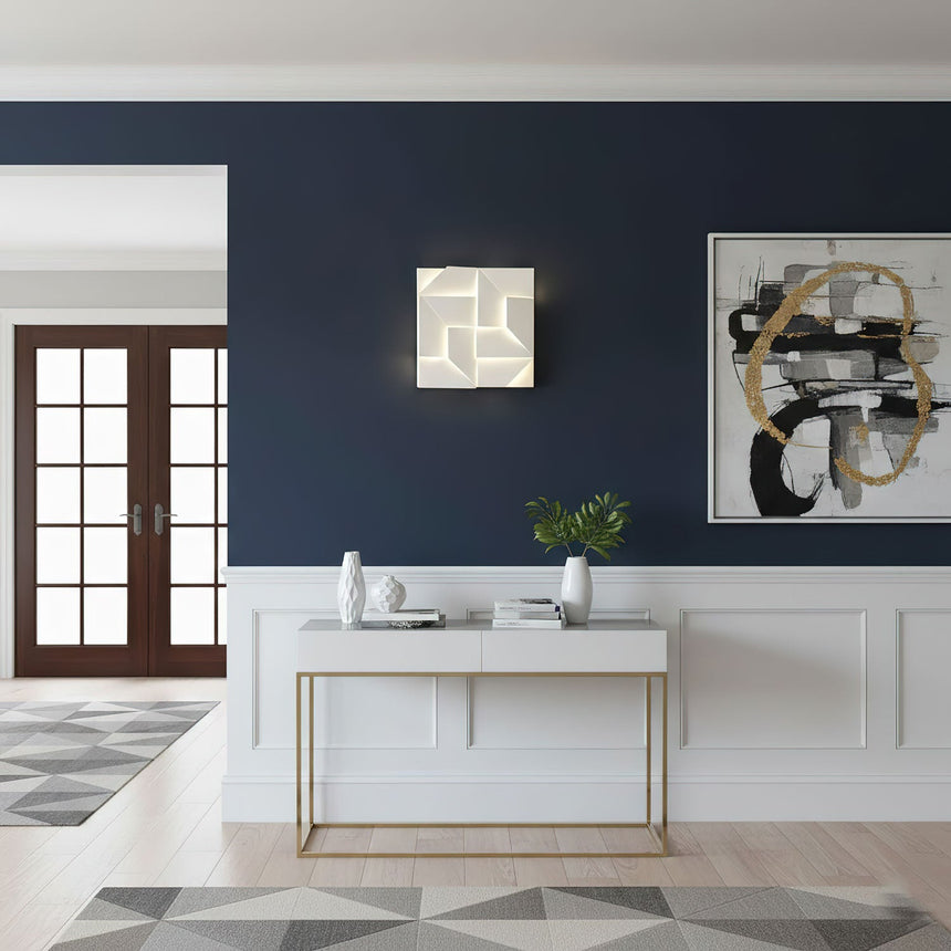 Lit on a navy wall above a white console with a vase and a framed artwork