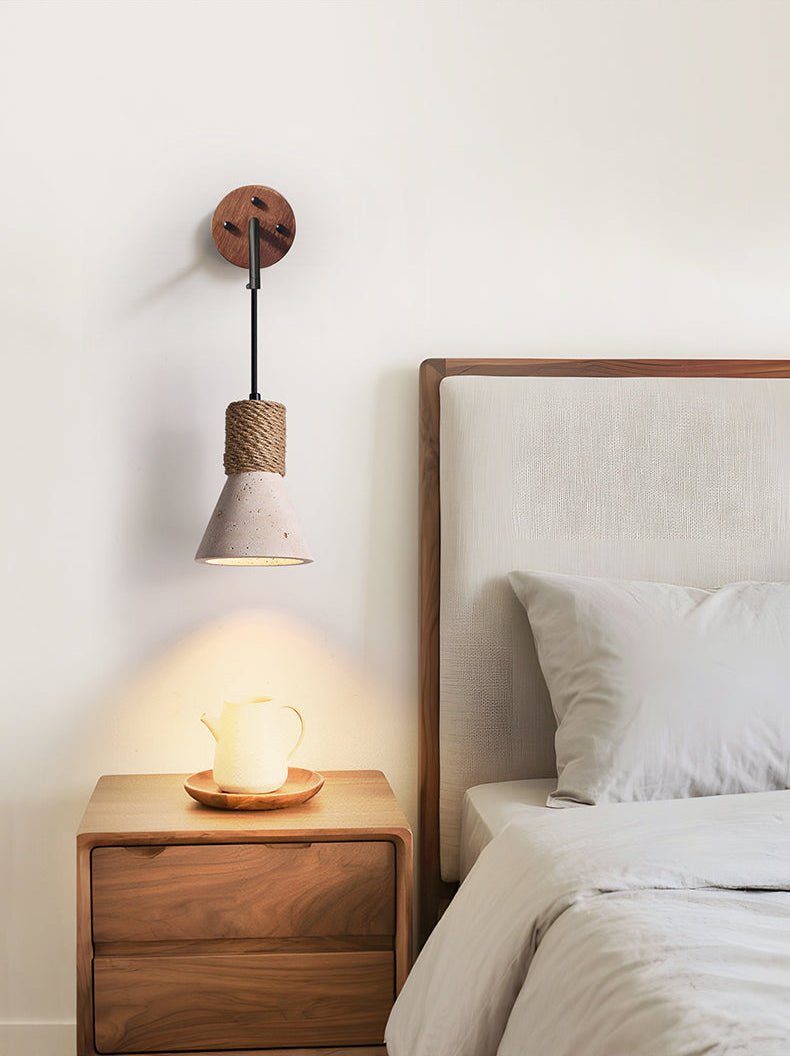 The cone light above a walnut nightstand with a cup, beside a pillow